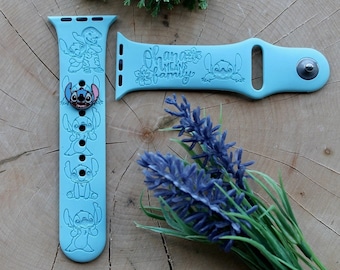 Può includere: Un cinturino per Apple Watch in silicone blu chiaro con un design a personaggio Stitch. Il cinturino ha il testo "Ohana means family". Il cinturino è mostrato con un ciondolo Stitch separato.