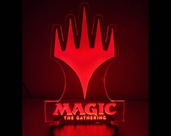 May include: A red LED night light shaped like the Magic: The Gathering symbol. The symbol is a five-pointed star with a diamond in the center. The words "Magic: The Gathering" are printed below the symbol.