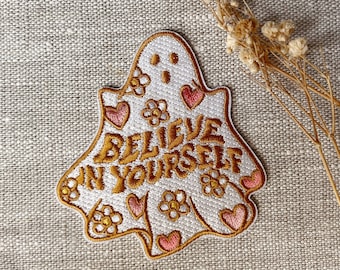 May include: White embroidered iron-on patch shaped like a ghost with the text "Believe in Yourself" in gold thread. The ghost is decorated with pink hearts and yellow flowers.