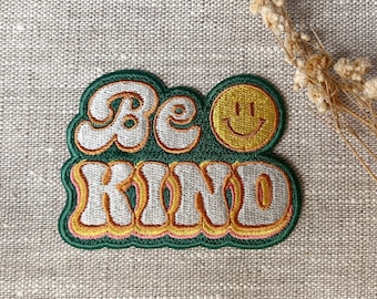 May include: Green, yellow, and white embroidered patch with the text "Be Kind" in a retro font. A yellow smiley face is next to the word "Be".