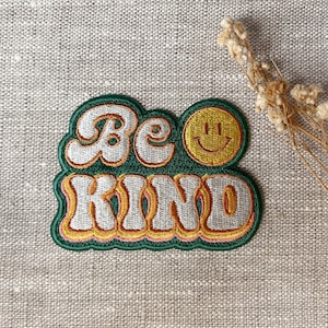 May include: Green, yellow, and white embroidered patch with the text "Be Kind" in a retro font. A yellow smiley face is next to the word "Be".