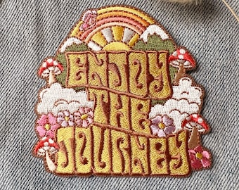 May include: Embroidered patch with a yellow, green, and pink design. The patch features a rainbow, clouds, mushrooms, and the text "Enjoy the Journey".