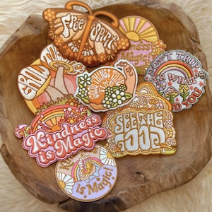 Puede incluir: Una colección de ocho parches bordados para planchar con una estética retro de los años 70. Los parches presentan varios diseños, incluyendo una mariposa, un caracol, un hongo, arcoíris y las palabras "Free Spirit", "Good Things Take Time", "Don't Trip", "See The Good", "Kindness is Magic" y "Kindness is Magic!"