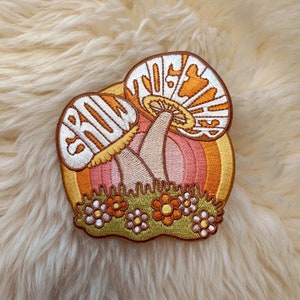 May include: Embroidered patch featuring two mushrooms with the words "Grow Together" in a retro style. The mushrooms are yellow and orange with white accents and are set against a pink and orange background with green foliage.