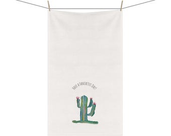 Puede incluir: Toalla blanca con una ilustración de cactus en acuarela y la frase "Have a Fancactus Day!". El cactus es verde con flores rosas. La toalla está colgada de un tendedero con dos pinzas de madera.
