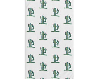 Puede incluir: Toalla rectangular blanca con un patrón repetido de cactus verdes y azules con flores rosas. Los cactus están estilizados y dispuestos en filas y columnas sobre la superficie de la toalla.