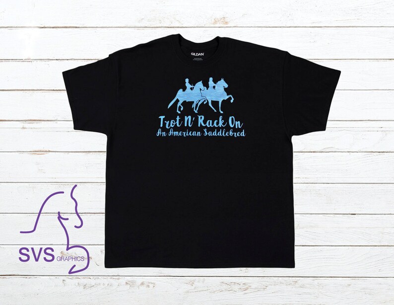 Op de afbeelding: Zwart T-shirt met een blauwe afbeelding van drie paarden en ruiters. De tekst "Trot N' Rack On An American Saddlebred" is onder de afbeelding gedrukt.