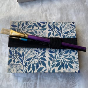 Floral watercolour sketchbook. Coptic binding with 300gsm cold pressed paper. Front view of A5 landscape book. With elastic tie which can also hold pencils or bruches.