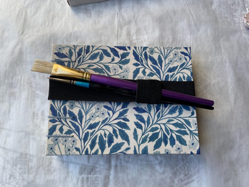 Floral watercolour sketchbook. Coptic binding with 300gsm cold pressed paper. Front view of A5 landscape book. With elastic tie which can also hold pencils or bruches.