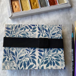 Floral watercolour sketchbook. Coptic binding with 300gsm cold pressed paper. Front view of A6 landscape book with elastic tie.