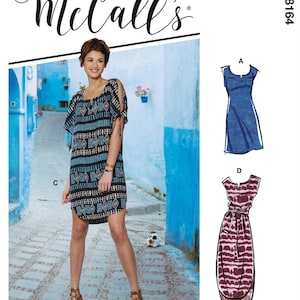 May include: A woman wearing a black, blue, and tan patterned dress with cut-out sleeves. The dress is paired with brown heels. The image also features a McCall's pattern with illustrations of two dress designs. The background is a blue-walled alley.