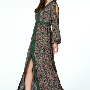May include: A long, floral-print dress with a V-neck and long sleeves. The dress features a dark background with a pattern of pink and peach flowers. Green lace trim accents the neckline, waist, and slit. The dress is paired with tan high-heeled sandals.