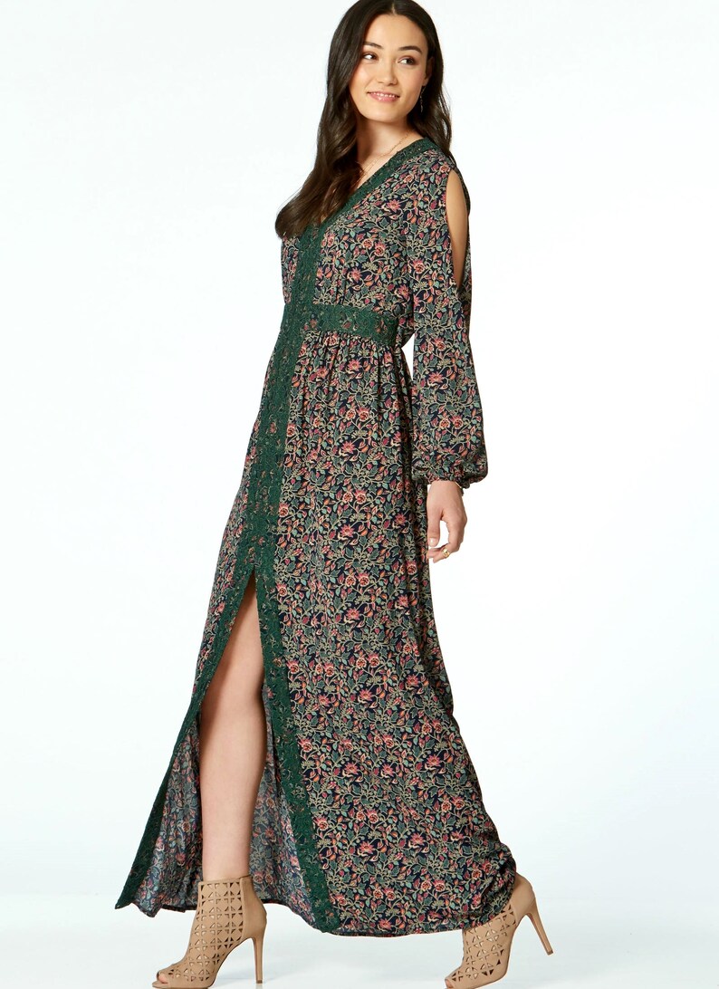 May include: A long, floral-print dress with a V-neck and long sleeves. The dress features a dark background with a pattern of pink and peach flowers. Green lace trim accents the neckline, waist, and slit. The dress is paired with tan high-heeled sandals.