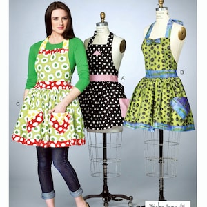 May include: Three different apron designs with polka dot patterns. The aprons are green, black and white, and green and blue. The aprons are all on mannequins and a person is wearing the green and red apron. The pattern on the green and red apron is a green background with red and yellow circles. The pattern on the black and white apron is black with white polka dots. The pattern on the green and blue apron is green with blue polka dots. The aprons are all made by TrishaJane and the pattern number is M7208.