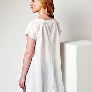 May include: White cotton top with a ruffled hem and short sleeves. The top has a scoop neck and a dotted pattern.