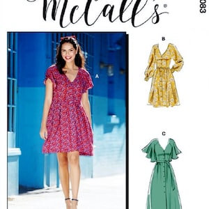 May include: McCall's sewing pattern M8083 for a dress with three different views. View A shows a woman wearing a red floral print dress with short sleeves. View B shows a yellow floral print dress with long sleeves and a tie belt. View C shows a green dress with short, ruffled sleeves and a tie belt.