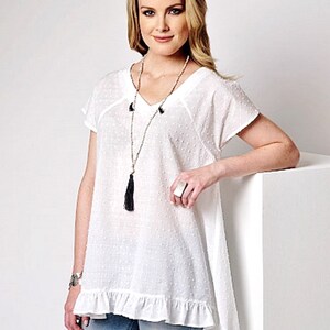May include: White cotton top with a v-neck, short sleeves, and a ruffled hem. The top has a dotted pattern and a black tassel necklace.