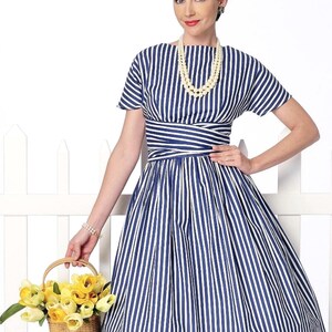 May include: A woman wearing a blue and white striped dress with a white pearl necklace. She is holding a basket of yellow flowers.