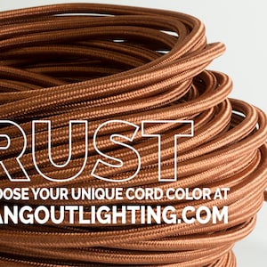 May include: Close-up of a spool of copper-colored electrical cord. The cord is tightly wound and has a smooth, shiny finish. The text "RUST" is superimposed over the cord in white letters. The text "CHOOSE YOUR UNIQUE CORD COLOR AT HANGOUTLIGHTING.COM" is below the cord.