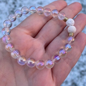 May include: A bracelet made with iridescent clear glass beads and two white lava rock beads with gold spacers.