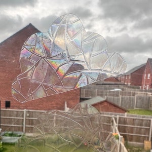 May include: Two iridescent window clings in the shape of clouds. The clings have a geometric pattern and are made of a clear, translucent material.