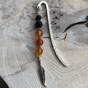 May include: Silver bookmark with a feather charm and a string of beads. The beads are black lava stone and orange carnelian.