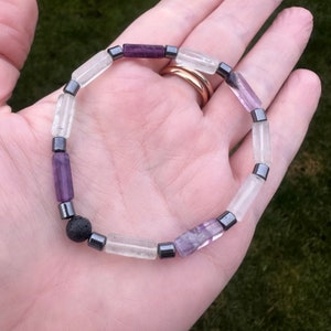 May include: A bracelet made with clear, white, and purple beads, interspersed with black hematite beads and a black lava bead.