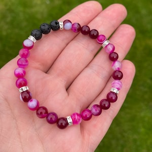 May include: A pink and white agate gemstone bracelet with silver spacers and black lava beads.