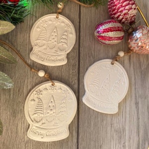 May include: Three white ceramic ornaments shaped like snow globes with three gnomes inside each globe. Each ornament has the text "Merry Christmas" on the bottom.