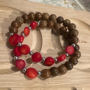 May include: A double-strand bracelet featuring red coral beads and brown wooden beads. The bracelet is crafted from natural materials and has a simple, elegant design.