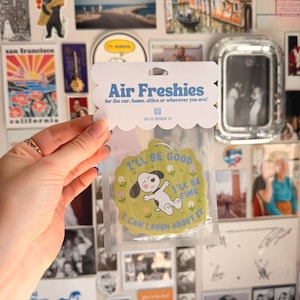 May include: A light green, scalloped-edge air freshener in a clear plastic sleeve with a header card that reads Air Freshies for the car, home, office or wherever you are! The freshener features a cartoon dog and the text I'll be good, I'll be fine, I can laugh about it.