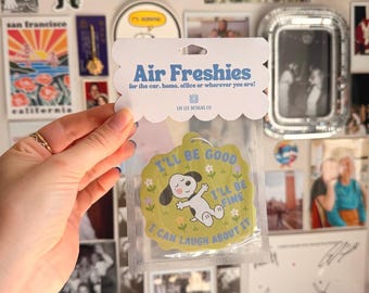 May include: A light green, scalloped-edge air freshener in a clear plastic sleeve with a header card that reads Air Freshies for the car, home, office or wherever you are! The freshener features a cartoon dog and the text I'll be good, I'll be fine, I can laugh about it.