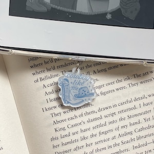 Puede incluir: Un charm de acrílico azul claro con temática de vaquero. El charm presenta una bota de vaquero, un sombrero de vaquero y el texto "cowboy like me". El charm está sujeto a una funda transparente para teléfono.