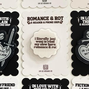 May include: A circular e-reader and phone grip with a scalloped edge, featuring a light beige checkered background and the dark brown text: i literally just want to read my slow burn romance & rot. The grip is mounted on a white scalloped display card.