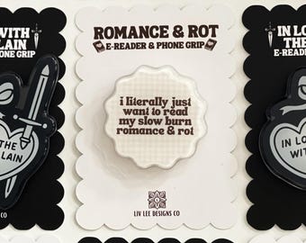 Può includere: Un supporto circolare per e-reader e telefono con bordo smerlato, caratterizzato da uno sfondo a quadretti beige chiaro e dal testo marrone scuro: i literally just want to read my slow burn romance & rot. Il supporto è fissato su una carta bianca.