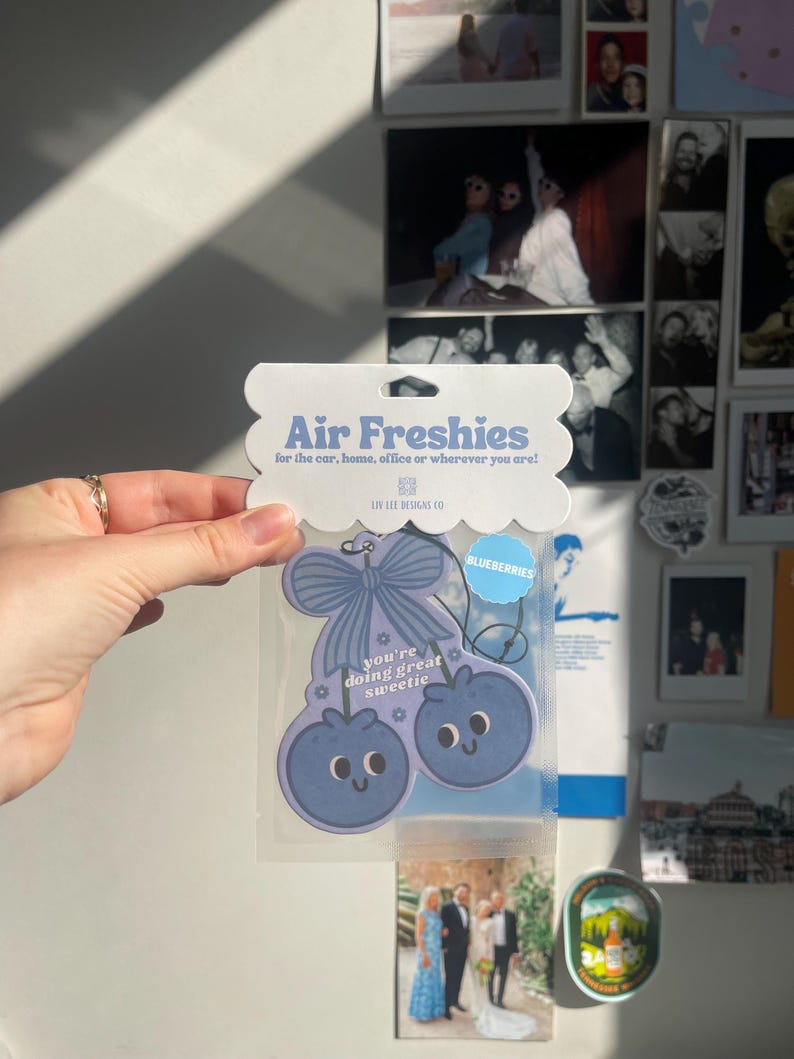 May include: Blueberry-shaped air freshener with the text "Air Freshies" and "you're doing great sweetie." The air freshener is light blue with a bow and two blueberries with smiling faces. The packaging says "for the car, home, office or wherever you are!"