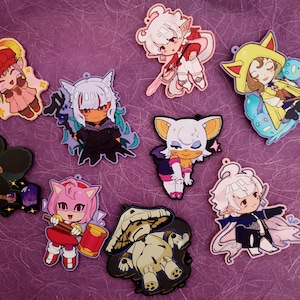 Peut inclure: Un ensemble de neuf porte-clés de personnages de dessins animés colorés. Les personnages sont dessinés dans un style chibi et comprennent un hérisson rose, un chat noir, un lapin blanc, un chien jaune, une chauve-souris violette, un champignon vert, un elfe bleu, un elfe rouge et un elfe blanc.