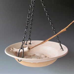 May include: A white ceramic bird feeder with a twig perch and a black chain for hanging.