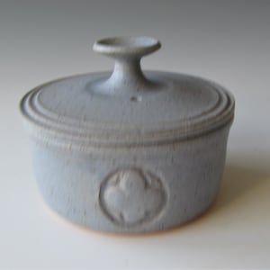 May include: A light blue ceramic lidded dish with a raised design on the lid and a decorative design on the side.