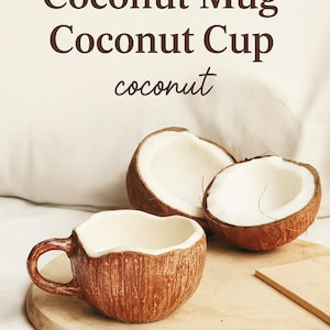 May include: A brown coconut shell mug with a white interior. The mug is sitting on a wooden cutting board. Two halves of a coconut are also visible in the image.