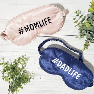 May include: Two satin sleep masks, one pink with the text "#MOMLIFE" and one navy blue with the text "#DADLIFE".