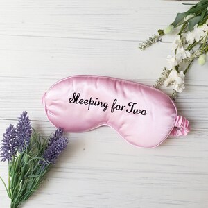 May include: Pink satin sleep mask with the text "Sleeping for Two" embroidered in black.