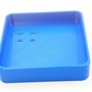 May include: A small, square, blue plastic tray with four small holes in the bottom.