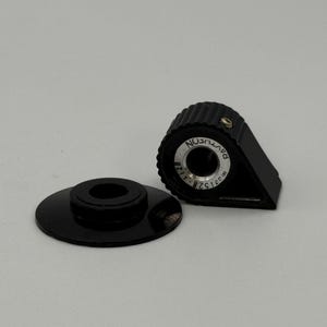 May include: Two black plastic components. One is a circular base with a central hole, and the other is a triangular piece with a ridged top and a circular inset with text. The text reads "DAVTICON" and "82515-1128".