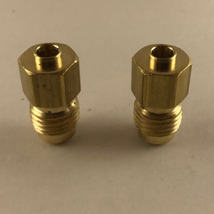 May include: Two brass fittings with a hexagonal top and threaded base. The fittings are a shiny gold color and appear to be new. They are likely used for plumbing or mechanical applications.
