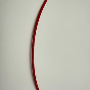 May include: A curved, bright red wire against a white background. The wire has the text "GEORIS, INC. ROCHESTER" printed along its length. The wire is likely electrical or for another technical application.
