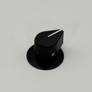 May include: A black control knob with a white indicator line. The knob has a ridged cylindrical base and a triangular top. It is mounted on a circular black base, suitable for electronic devices.