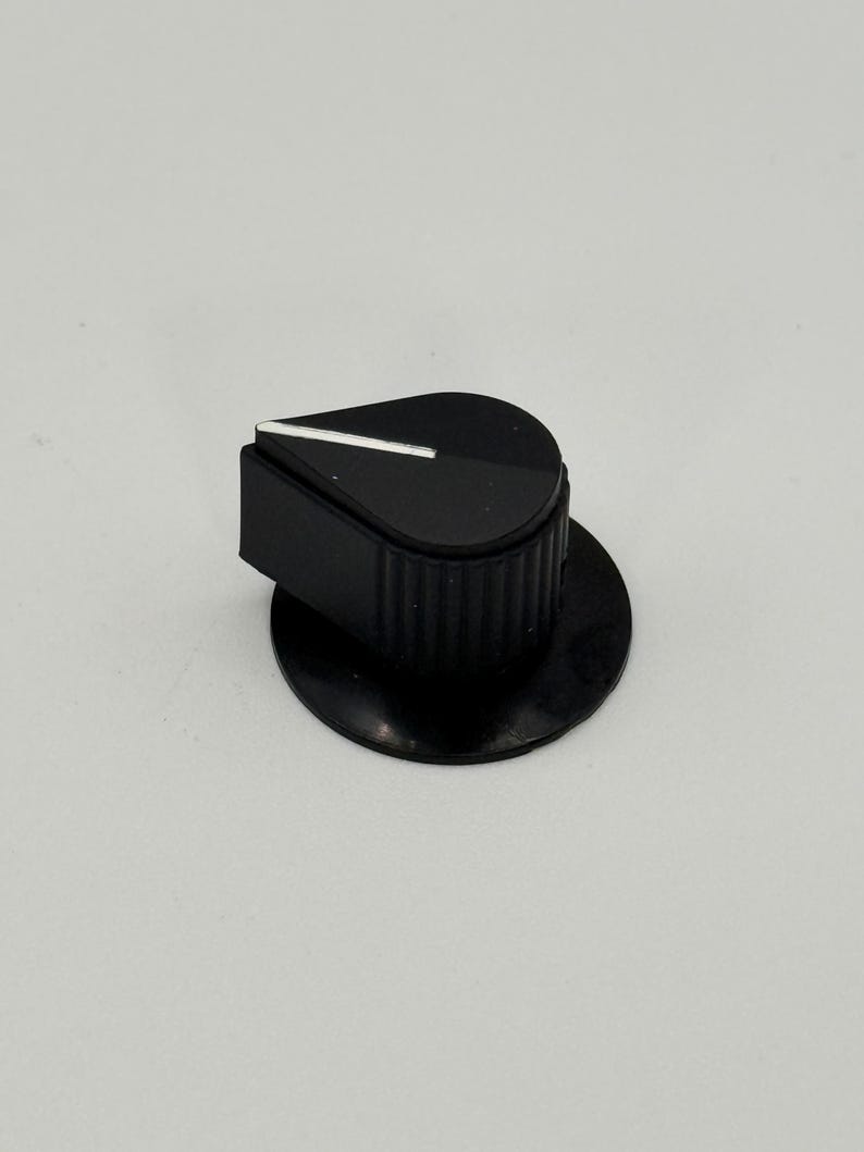 May include: A black control knob with a white indicator line. The knob has a rounded top and a ridged base, sitting on a circular base. The image is a close-up shot against a plain white background. This component is likely for electronics or audio equipment.