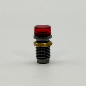 May include: A cylindrical indicator light component featuring a translucent red plastic cap at the top, a metallic gold-colored hexagonal nut, and a threaded dark grey metal body designed for secure mounting in electronic panels or machinery.