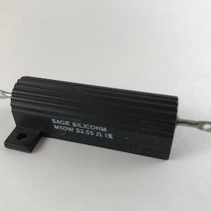 May include: A black, rectangular resistor with a ribbed surface. The resistor has two silver leads and is labeled "SAGE SILICOHM M50W 22.55 Ω 1X".